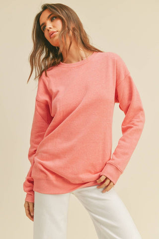 Woman wearing a rose pink sweatshirt and white pants against a beige background